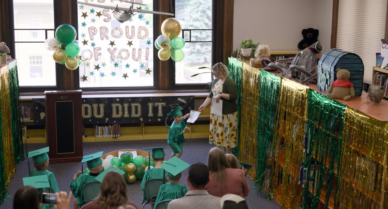 child in green cap and gown get a paper certificate